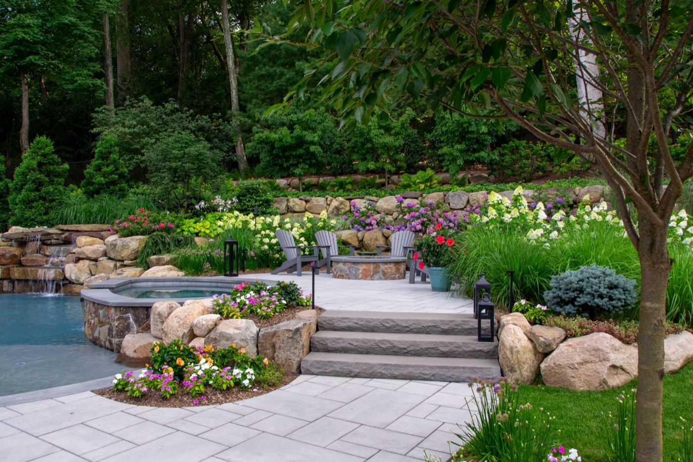 Landscaped backyard patio with pool, stone retaining walls, and flower beds by F.O.M. Landscaping